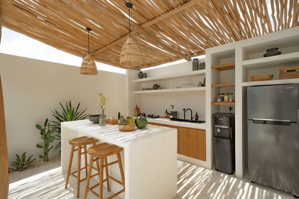 This one-bedroom vacation home is a serene coastal retreat that perfectly embodies the laid-back charm of island tropical living. The architecture showcases a harmonious blend of traditional island design with modern simplicity, creating a space that feels both stylish and inviting. The exterior features natural materials like exposed stone walls and wooden accents, reminiscent of classic island bungalows but with a contemporary twist. The open-plan layout maximizes natural light and airflow, with large windows and sliding glass doors that blur the lines between indoor and outdoor living. A private patio offers a peaceful spot to unwind, surrounded by lush greenery that adds to the home’s tranquil vibe. Inside, the interior design embraces a modern organic style with coastal influences. Neutral tones dominate the color palette, with soft whites, beiges, and earthy browns creating a calming atmosphere. Textures play a key role here—think rattan pendant lights, woven jute rugs, and linen-upholstered furniture, all adding warmth and a touch of rustic charm. The bedroom is a cozy sanctuary with a canopy bed dressed in crisp, breathable fabrics. Simple yet elegant décor elements, like hand-carved wooden details and shell-adorned accessories, reflect the island’s coastal setting. The bathroom continues the natural theme with stone basins, rainfall showers, and smooth concrete surfaces, offering a spa-like experience. This vacation home is an ideal choice for travelers seeking a stylish yet comfortable base while exploring the island’s famous surf spots and stunning beaches. The design strikes a perfect balance between modern convenience and tropical aesthetics, making it a quintessential island getaway.