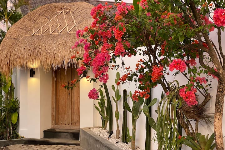 Area parkir luas dan gerbang masuk depan dengan bunga tropis