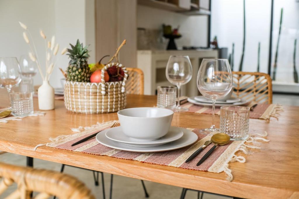 a wooden table with a bowl and plates and wine glasses at Villa Naia Berawa in Canggu